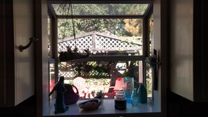 Une fenêtre donnant sur une terrasse en bois, avec une plante suspendue et divers objets placés sur le rebord de la fenêtre, notamment un bol, un bocal et une bouteille.