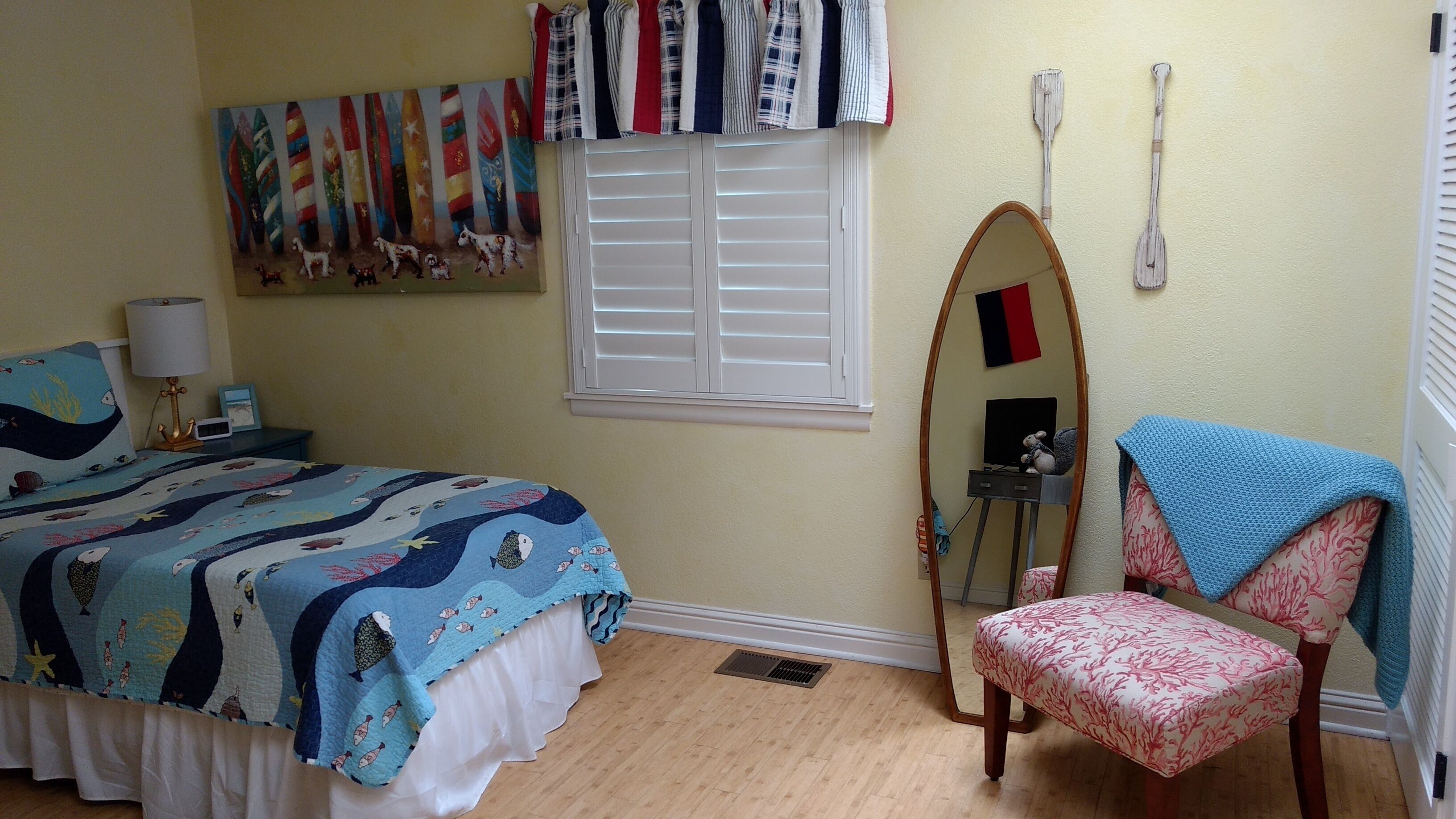 Quarto com cama, cadeira, janela com persianas, quadro e espelho.