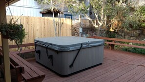 A hot tub on a wooden deck with a wooden fence and a stone wall in the background. - Charming Remodeled Single Level. HotTub. Fenced backyard. Porch view! (Cambria)