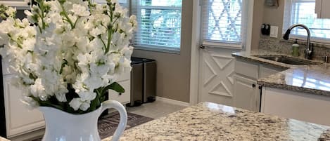 A kitchen with a granite countertop, a white pitcher with flowers, a starfish, and a sign that says "Let's Do Sunset".