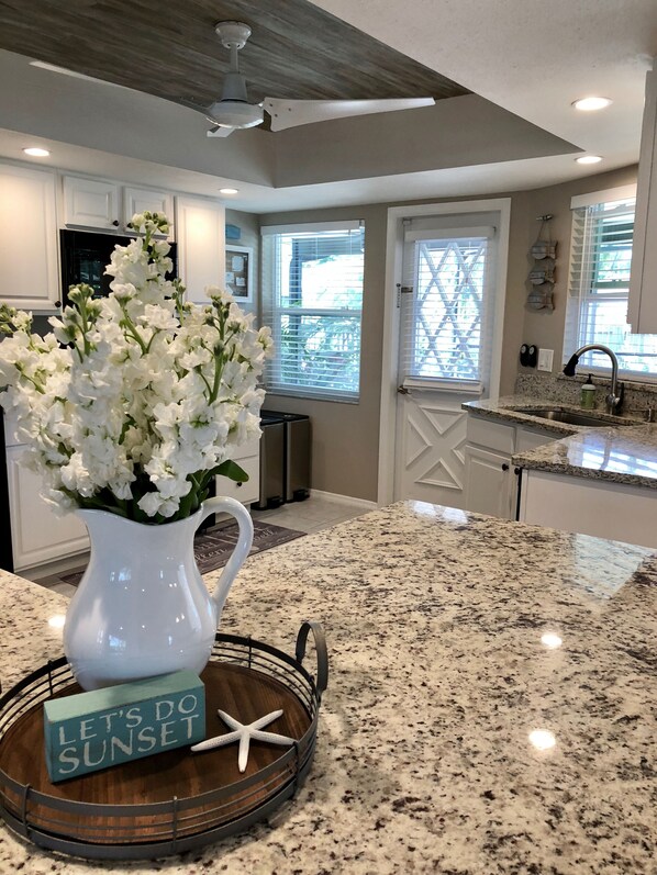 A kitchen with a granite countertop, a white pitcher with flowers, a starfish, and a sign that says "Let's Do Sunset".
