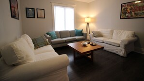 A living room with two white sofas, a wooden coffee table, and a floor lamp. - ♥ Maison Doucet Property | New Standard Rental | Niagara Falls ♥ (Niagara Falls)
