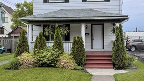 A two-story house with a front porch, a small garden with shrubs, and a red front door. - ♥ Maison Doucet Property | New Standard Rental | Niagara Falls ♥ (Niagara Falls)