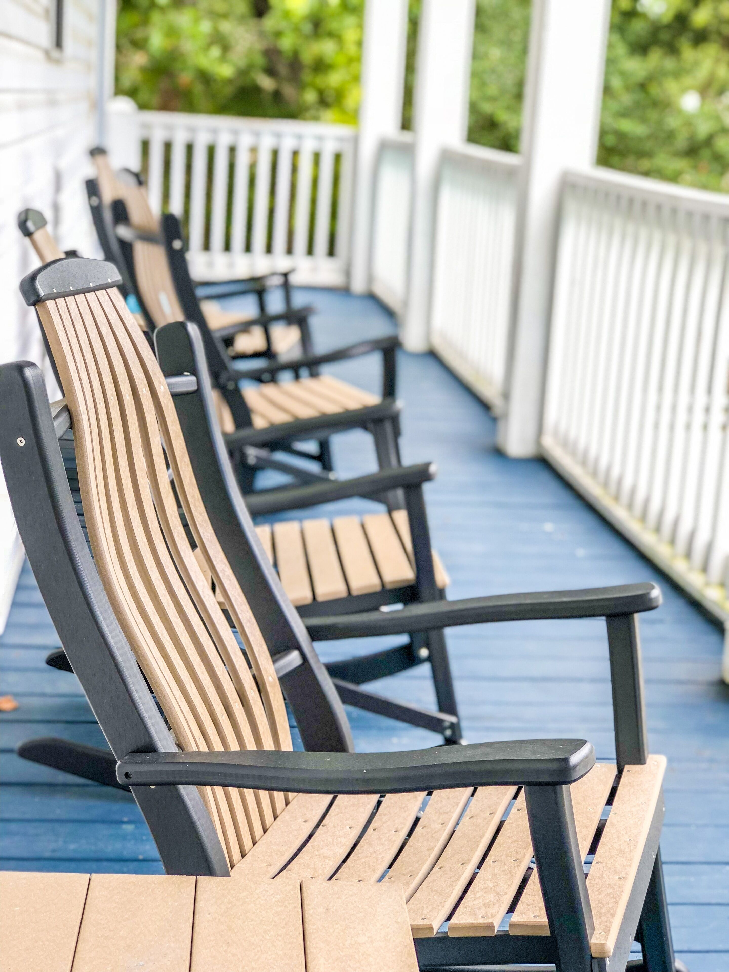 Rivi Adirondack-tyylisiä puutarhatuoleja puukannella, jossa on valkoiset kaiteet.
