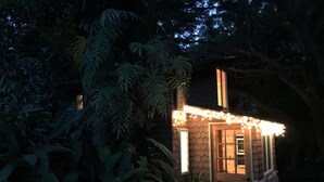 A small, rustic cabin with a stone exterior and a wooden door, surrounded by dense foliage.