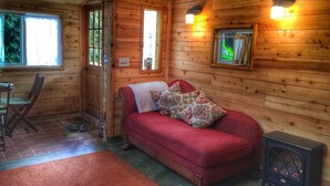 A cozy cabin interior with a red sofa, wooden walls, and a fireplace.