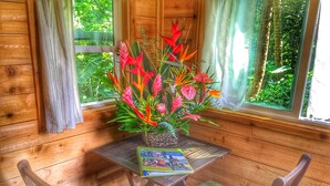 A wooden cabin interior with a table, chairs, a book, and a floral arrangement.