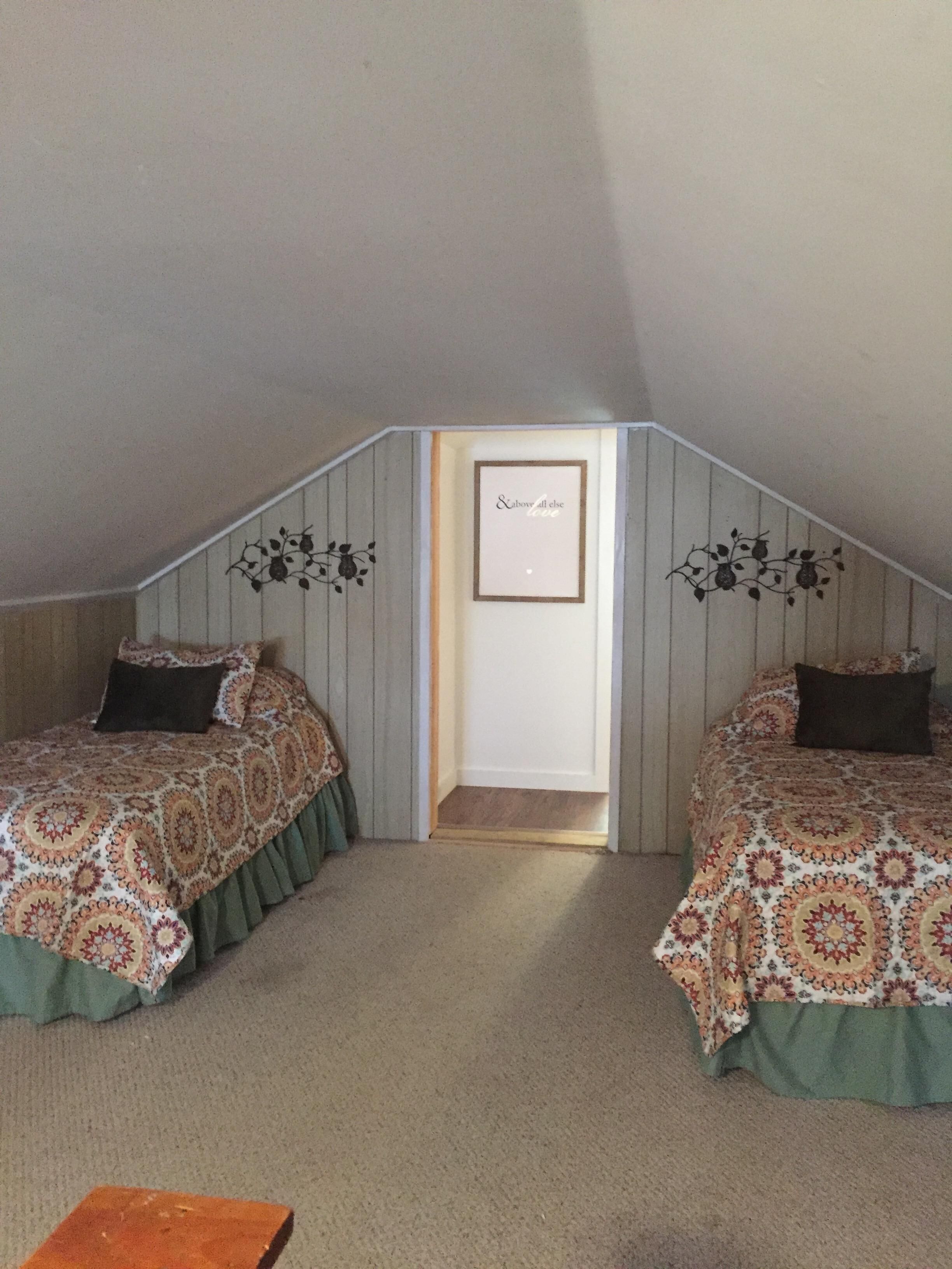 A small, triangular attic bedroom with two beds, a door, and decorative wall art.