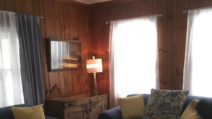 Ein gemütliches Wohnzimmer mit Holzwänden, einem blauen Sofa mit gelben Kissen, einem Holztisch und einer Lampe auf einem Beistelltisch.