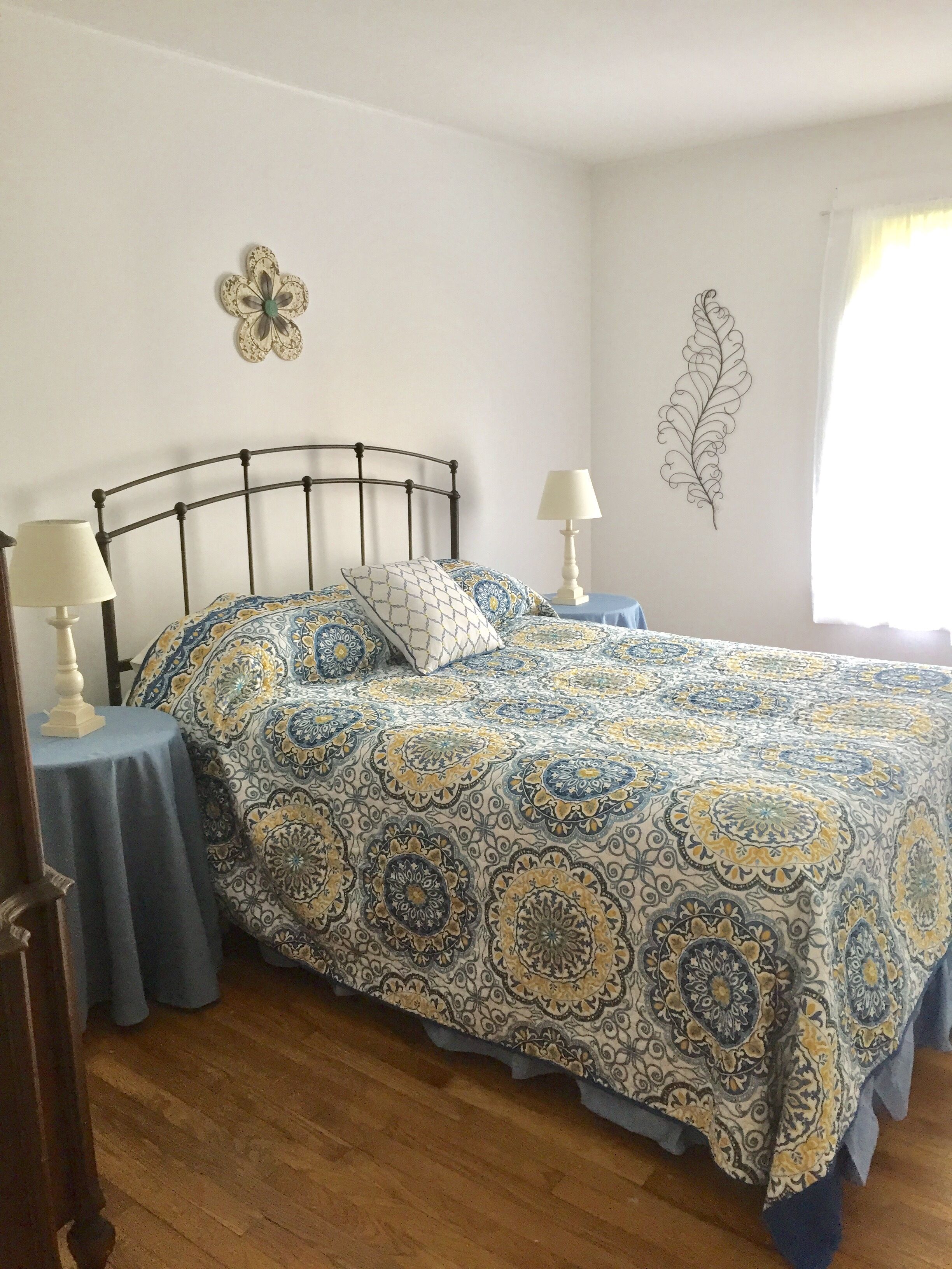 A bedroom with a metal bed frame, patterned bedspread, two bedside lamps, and decorative wall art.