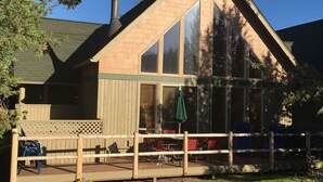 A two-story house with a large deck, a covered patio, and a fenced outdoor seating area. - Remodeled cozy cabin on golf course with hot tub!  (Redmond)