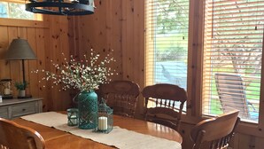 A wooden dining room with a round table, six chairs, a chandelier, and a window with blinds. - Remodeled cozy cabin on golf course with hot tub!  (Redmond)