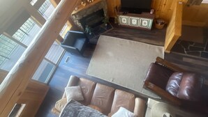 A wooden cabin interior with a stone fireplace, a television, and a sofa. - Remodeled cozy cabin on golf course with hot tub!  (Redmond)