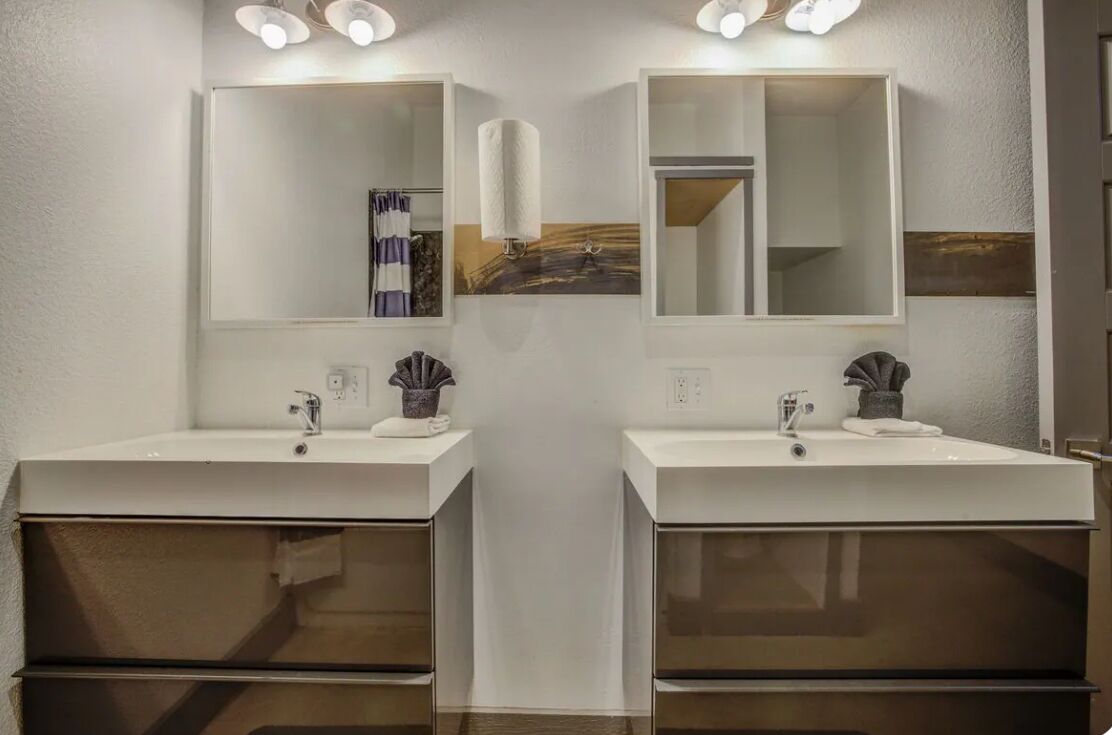 A bathroom with two sinks, each with a mirror above. There are wall-mounted lights above the mirrors.