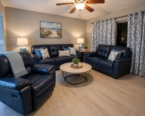 A living room with two leather sofas, a coffee table, and a ceiling fan. - Beautiful Spacious, 1500 SF, No Drive Beach, Heated Oceanfront Pool, Pets OK! (Daytona Beach Shores)