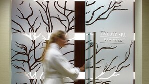 Una mujer con bata blanca abre una puerta decorada con un diseño de árbol y el letrero 
