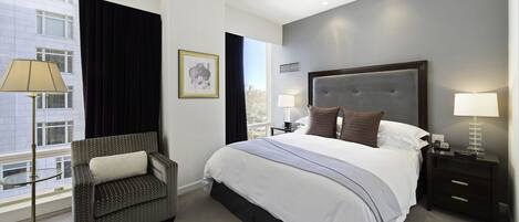 A modern hotel room with a large bed, a sitting area with a chair, a bedside table, and a view of the city.