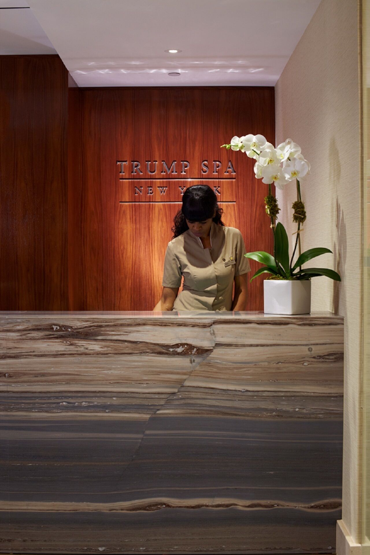 Un comptoir d’accueil, avec un mur en panneaux de bois derrière, sur lequel on peut lire l’inscription « TRUMP SPA NEW YORK ».