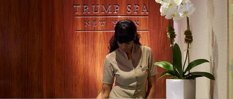 Un comptoir d’accueil, avec un mur en panneaux de bois derrière, sur lequel on peut lire l’inscription « TRUMP SPA NEW YORK ».