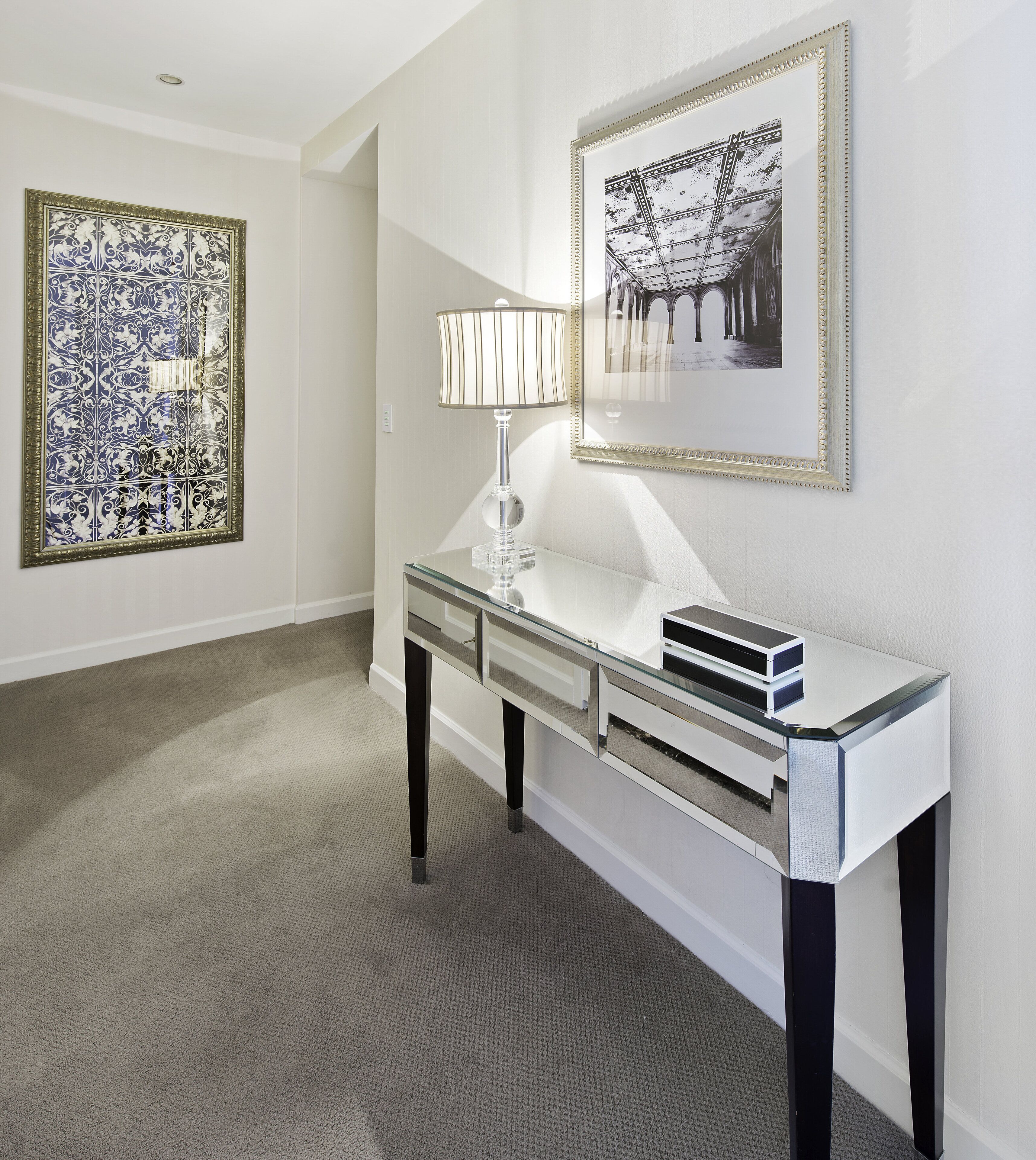 A modern room with a glass console table, a lamp, and two framed artworks on the wall.