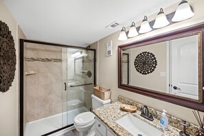 A bathroom with a glass-enclosed shower, a toilet, a sink with a granite countertop, and a large mirror with a decorative frame. - AMAZING VIEWS FROM THIS 2 BEDROOM 2 BATH BEACHSIDE CONDO  (Gulf Shores)