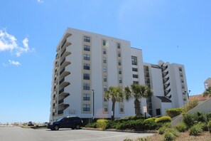 A multi-story hotel with a modern design, featuring balconies on each floor, a parking lot, and palm trees in the landscaping. - AMAZING VIEWS FROM THIS 2 BEDROOM 2 BATH BEACHSIDE CONDO  (Gulf Shores)