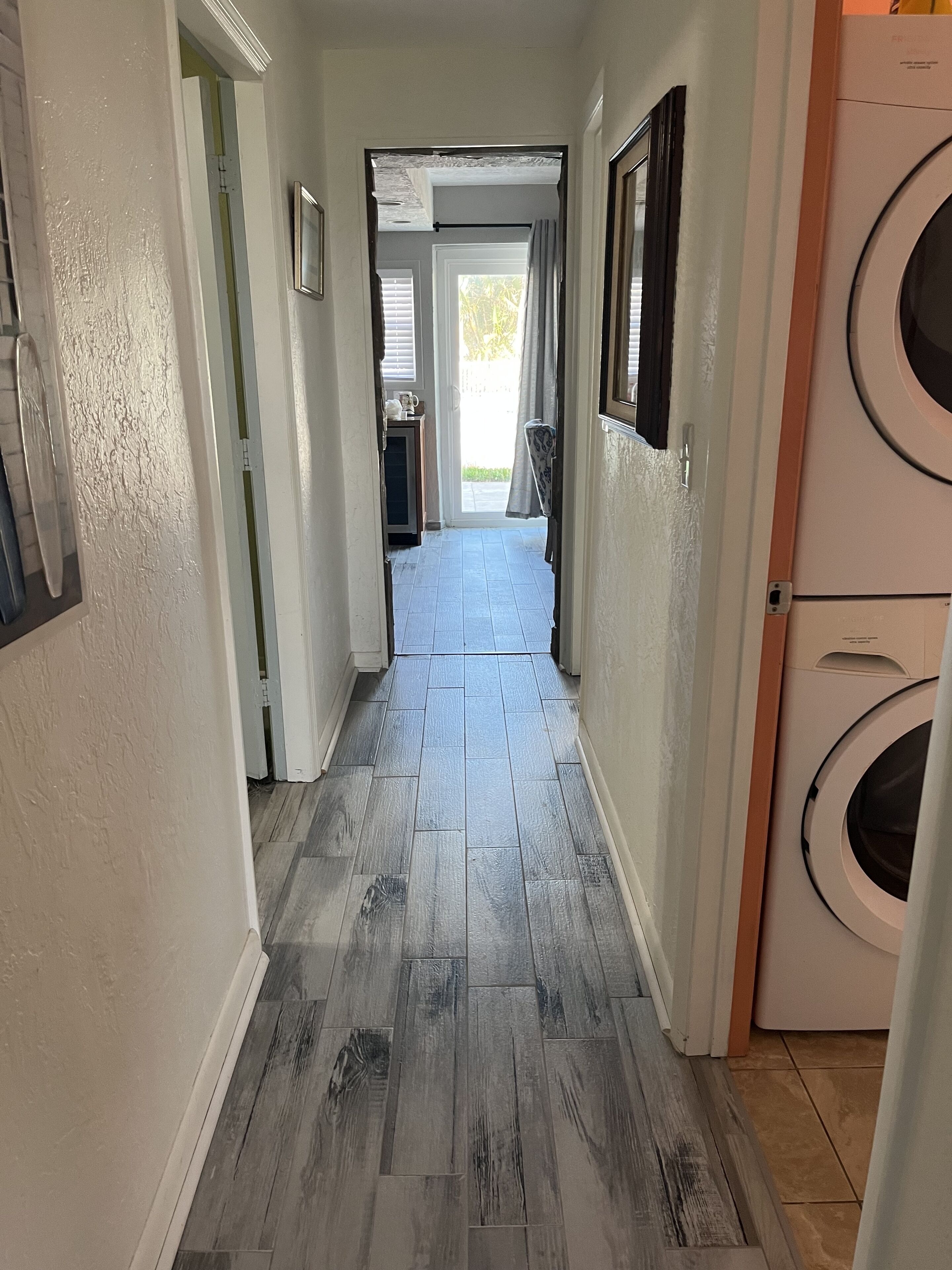 A hallway with grey wooden flooring, white walls, and a washing machine on the right.
