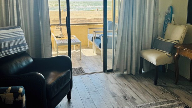 Ein Zimmer mit Blick auf den Strand, eine Schiebetür, ein Sofa, ein Sessel und ein kleiner Tisch.