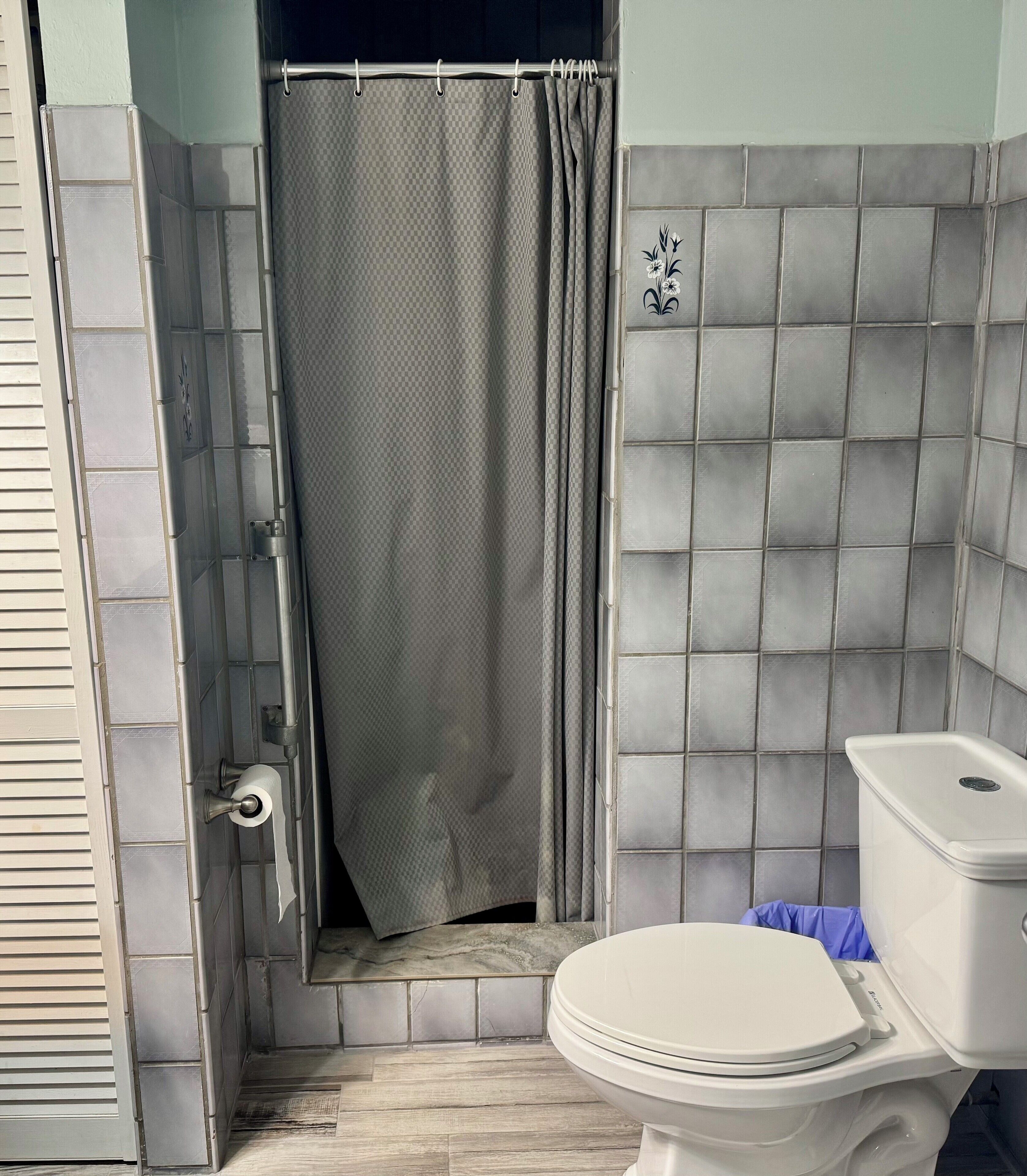 Une salle de bain avec des toilettes, un rideau de douche et des murs carrelés.
