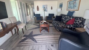 Ein geräumiges Wohnzimmer mit einem Teppich mit Seestern-Muster, einem Deckenventilator und einem großen Gemälde an der Wand.