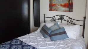 A bed with a patterned bedspread and pillows, a dark wardrobe, and a painting on the wall. -  LOVELY 1 Bedroom Apartment in the Heart of Golden (Golden)