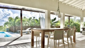 Un espace extérieur abrité, aménagé pour les repas, avec une piscine, une table en bois et des chaises.
