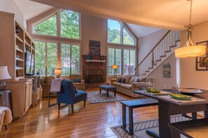 Un salón espacioso con chimenea, ventanas grandes y una escalera.