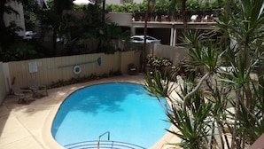 A swimming pool with a tiled deck, surrounded by palm trees and a wooden fence. - BOOK 30 DAYS OCT 15-NOV FREE PARKING! UNIT 52 WALK TO INTL MKT, TARGET, BEACH (Honolulu)
