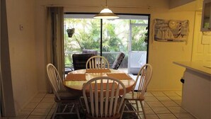 Comedor con una mesa redonda, cuatro sillas, una lámpara colgante y vistas al exterior a través de una puerta corrediza, donde se ven plantas.
