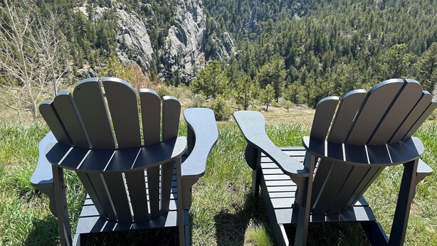 Kaksi Adirondack-tyylistä puutarhatuolia, jotka on sijoitettu niin, että ne osoittavat kohti vuoristoista maisemaa, jossa on kallioinen ulkonema ja tiheä metsä.