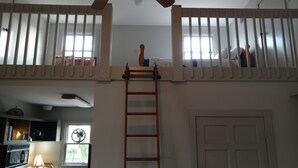 A room with a loft area featuring a wooden ladder leading to a balcony with white railings.