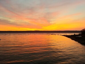 Solnedgang over et roligt vandareal med en kystlinje.