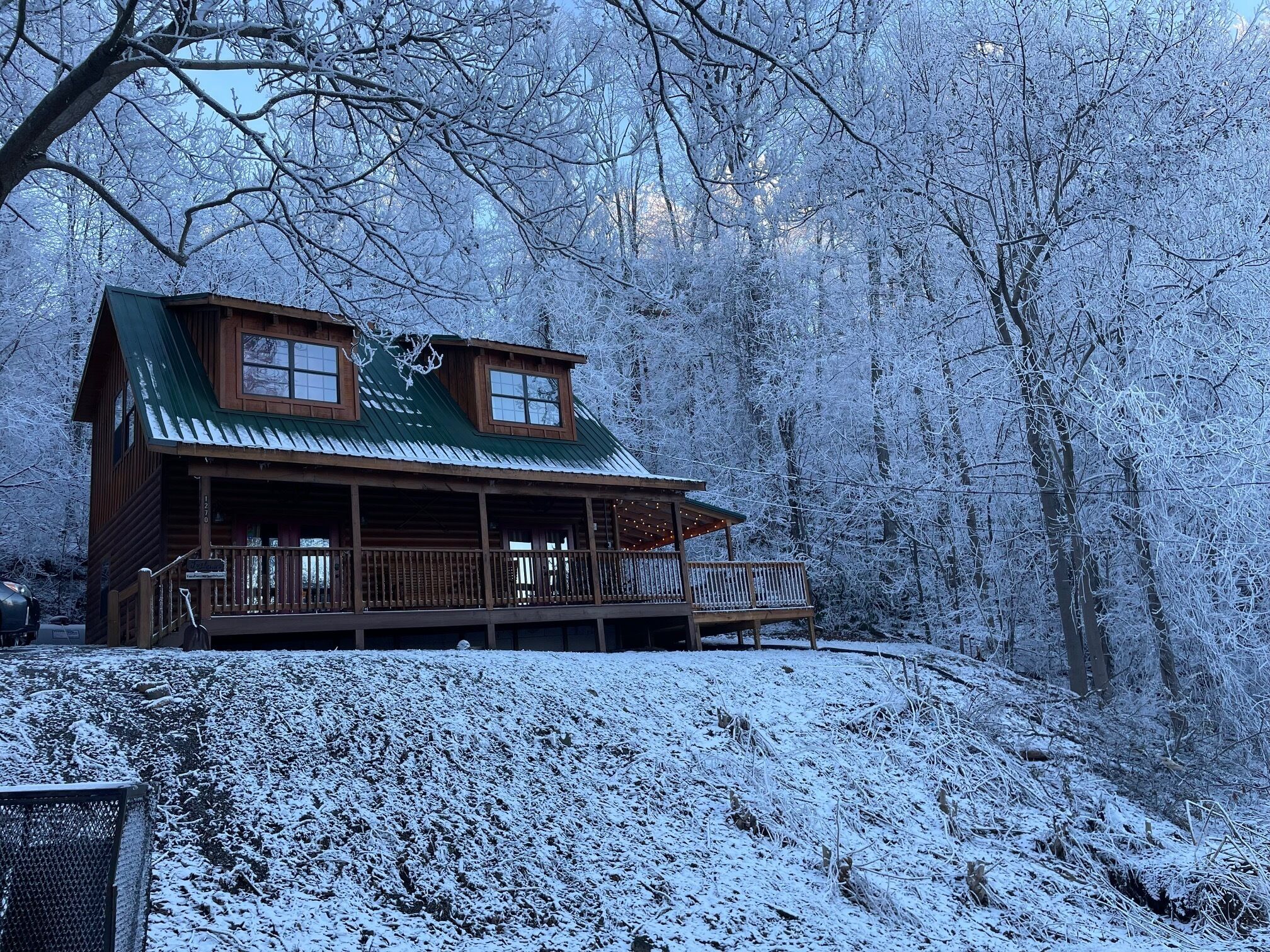 A wooden cabin with a green roof, a balcony, and a porch.