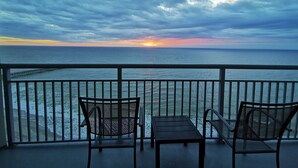 Un balcone con due sedie e un tavolo, affacciato su un tramonto sull'oceano.