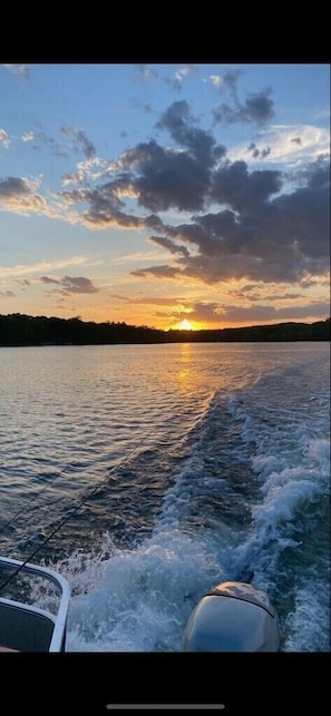 Un bateau sur une étendue d’eau, avec un coucher de soleil en arrière-plan.