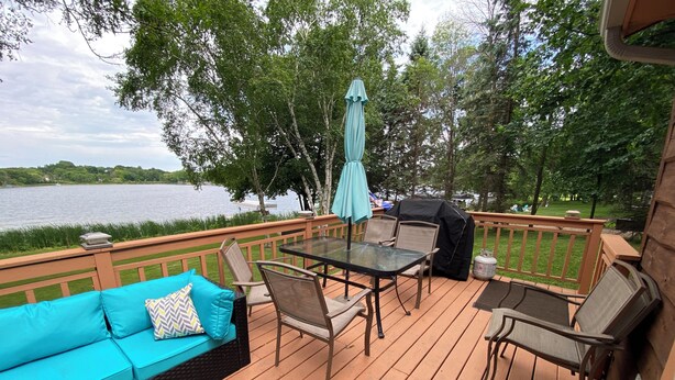 A wooden deck with a glass table and chairs, a blue sofa, and a grill.