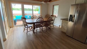A kitchen with a dining table, chairs, a refrigerator, and a view of a deck with outdoor furniture.