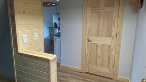 A wooden interior with a door, a staircase, and a kitchen in the background.
