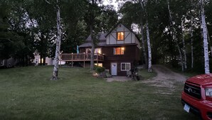 A two-story wooden cabin with a deck, surrounded by trees.