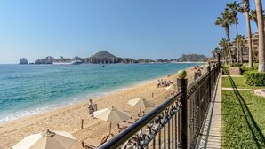 Une plage avec des parasols, une rambarde et des palmiers.