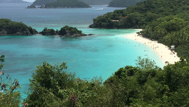 Un paisaje costero con una playa, aguas turquesas cristalinas y colinas verdes exuberantes.