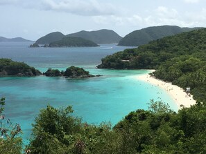 Un paisaje costero con aguas turquesas cristalinas, una playa arenosa y colinas verdes exuberantes.