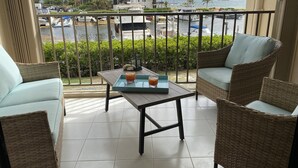 Un balcón con mobiliario de mimbre, una mesa con bebidas y vistas al puerto deportivo y edificios.
