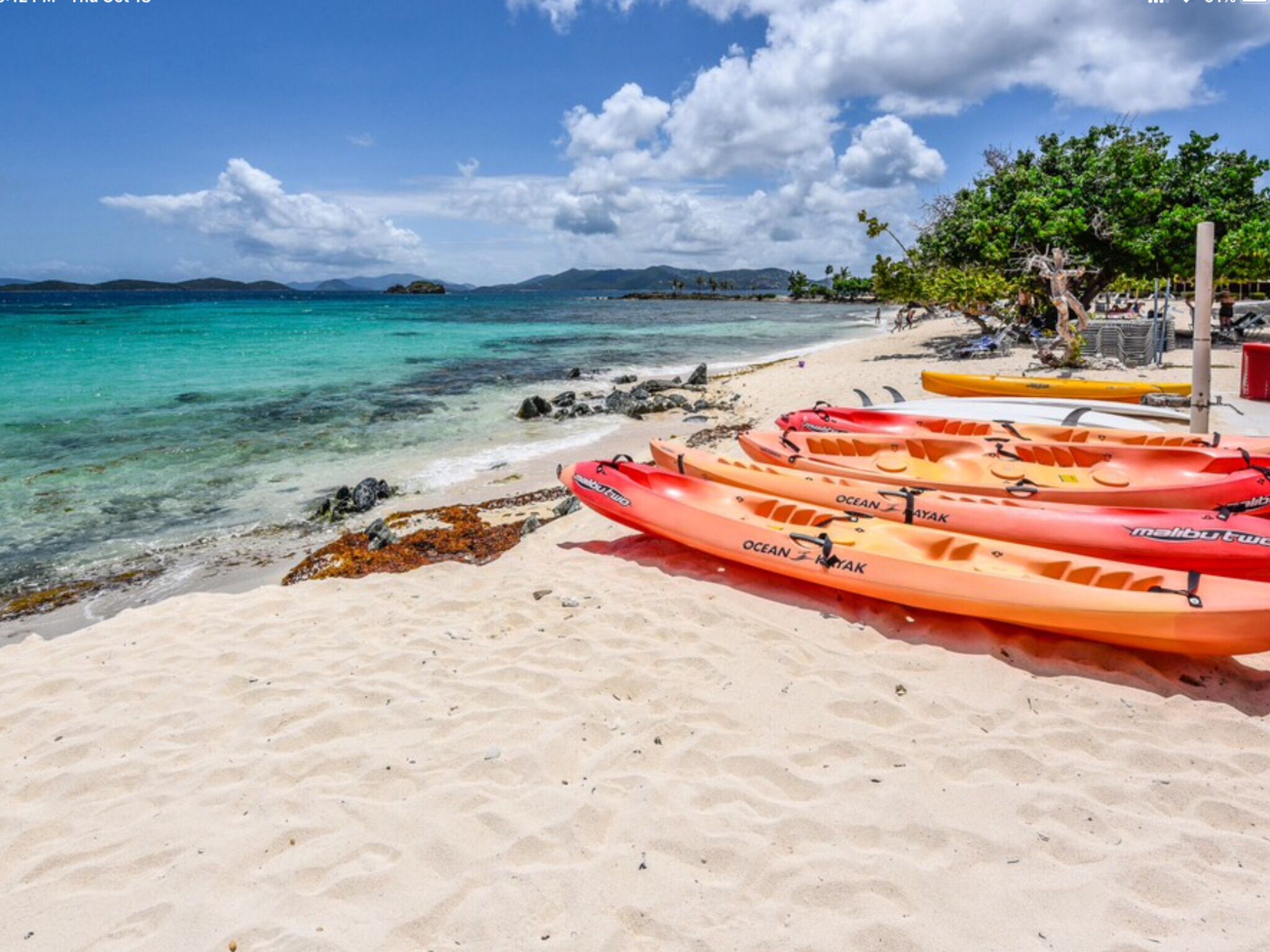 Una playa con kayaks alineados en la arena, cielo azul despejado y montañas a lo lejos.